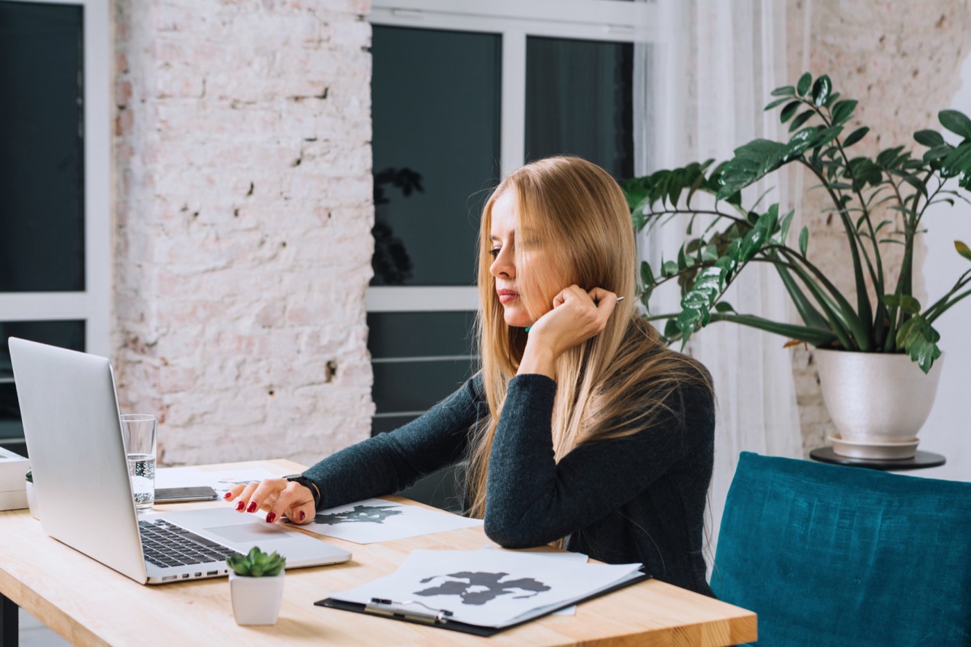 A woman working thoughtfully at her laptop in a bright home office