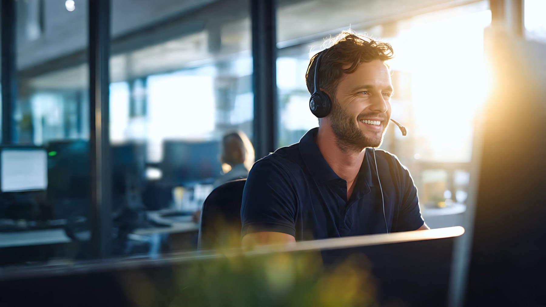A smiling adviser wearing a headset at his desk